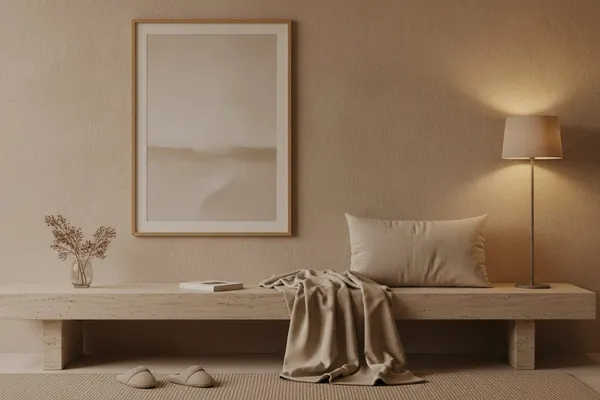 A calm living room corner with a large framed beige minimalist print centered above a low bench and a single soft lamp.