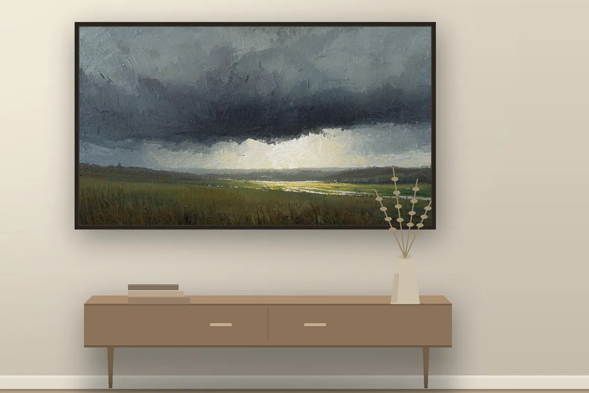 A Samsung Frame TV on a warm cream wall showing a quiet painterly landscape of a low storm over green fields, above a wooden console with a pale vase